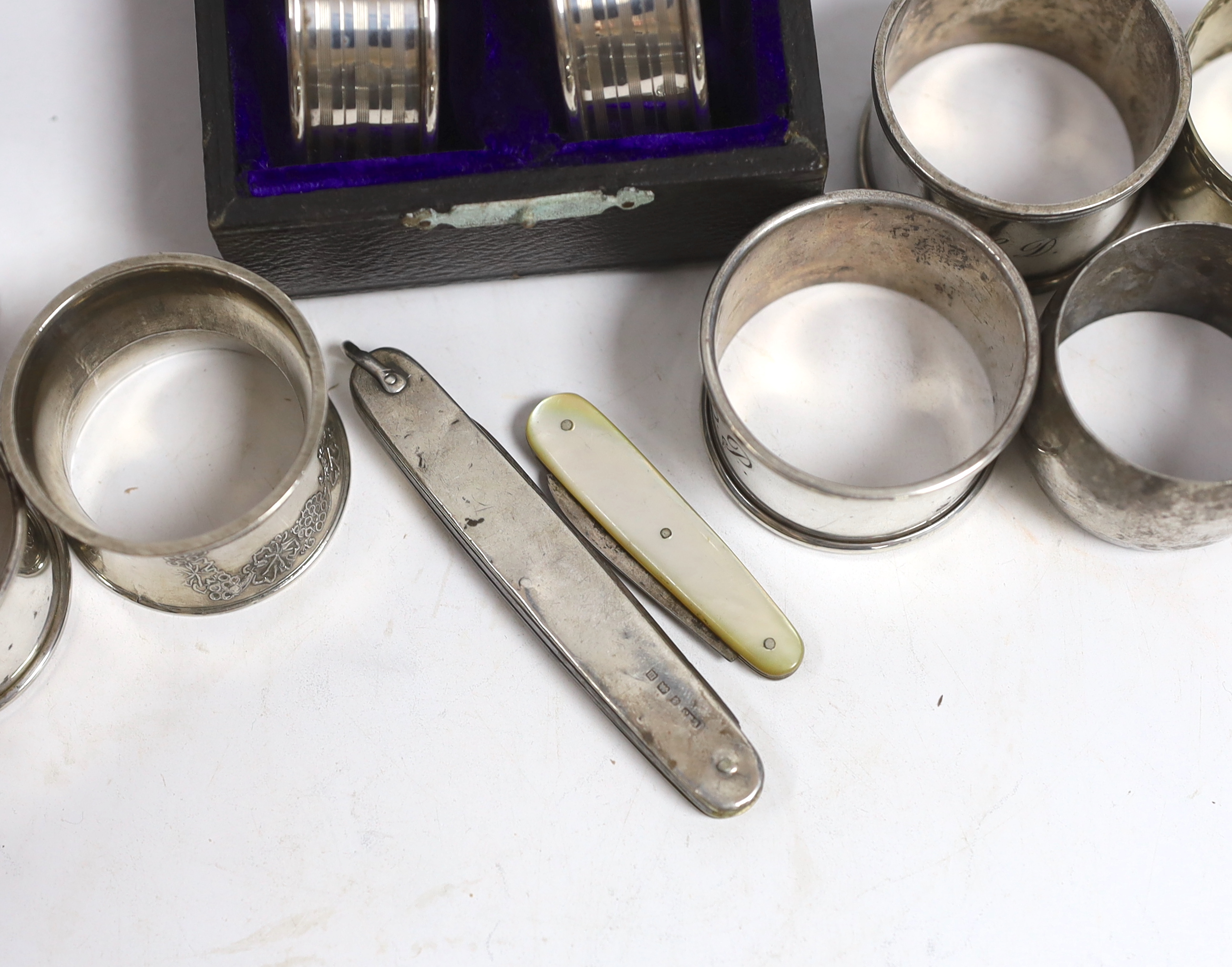 A cased set of four George V silver napkin rings, Rolason Brothers, Birmingham, 1920, together with five other assorted silver napkin rings, three plated napkin rings, two mother of pearl mounted fruit knives and a silve